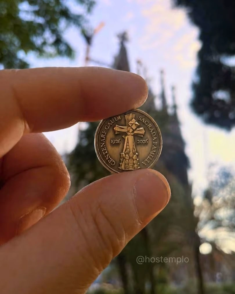 Medalla conmemorativa Gaudí 2026 Edición Hostemplo sostenida frente a la Sagrada Família de Barcelona.