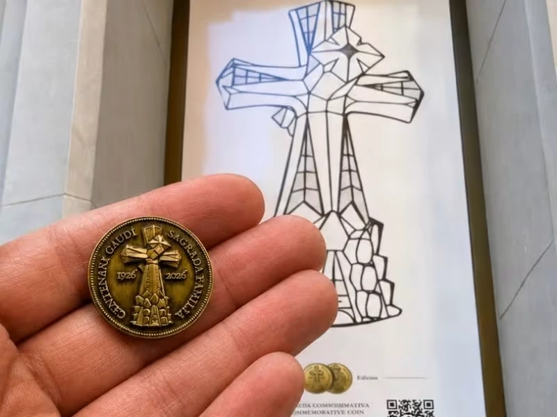 Medalla conmemorativa Gaudí 2026 en una mano frente al cartel del Centenari Gaudí en Hostemplo, junto a la Sagrada Família.