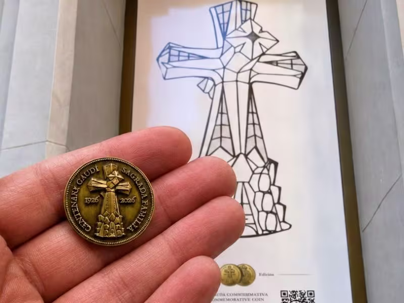 Medalla conmemorativa Gaudí 2026 en una mano frente al cartel del Centenari Gaudí en Hostemplo, junto a la Sagrada Família.