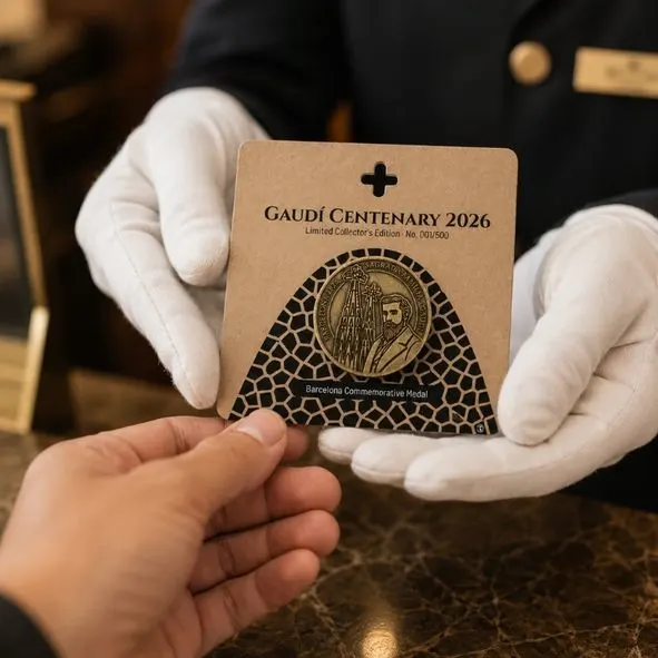 Recepcionista con guantes blancos entrega la Medalla Centenario Gaudí 2026 en blister kraft, edición limitada de Barcelona.