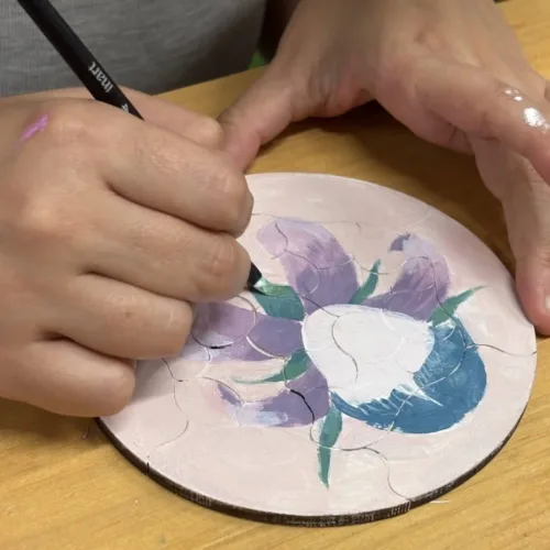 Detalle de una participante pintando flores sobre las piezas de madera del Puzzle Trencadís
