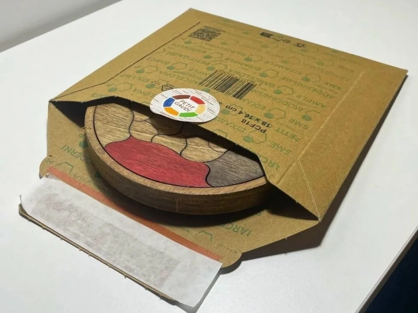 Puzzle Trencadís junto a su embalaje de cartón kraft y el material que lo protege.
