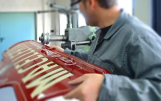 Artesano trabajando a mano un rótulo tradicional pintado en el taller de Rótulos Antiguos