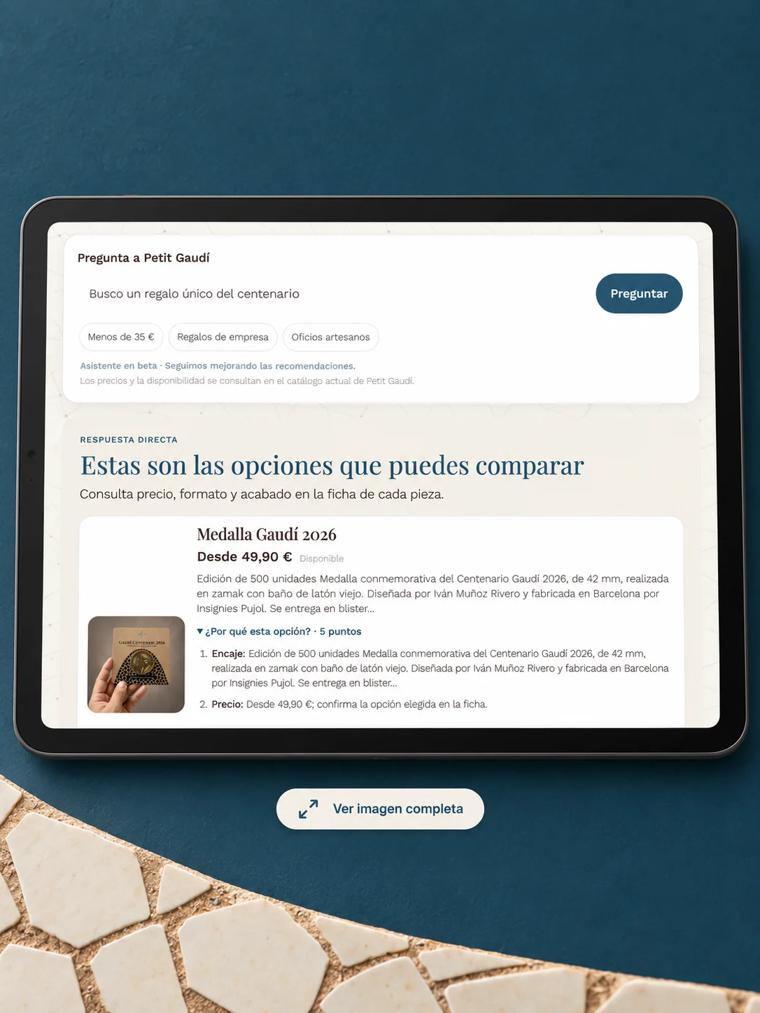Tablet con el asistente de Petit Gaudí recomendando la medalla Gaudí 2026, sobre fondo azul petróleo con trencadís marfil.