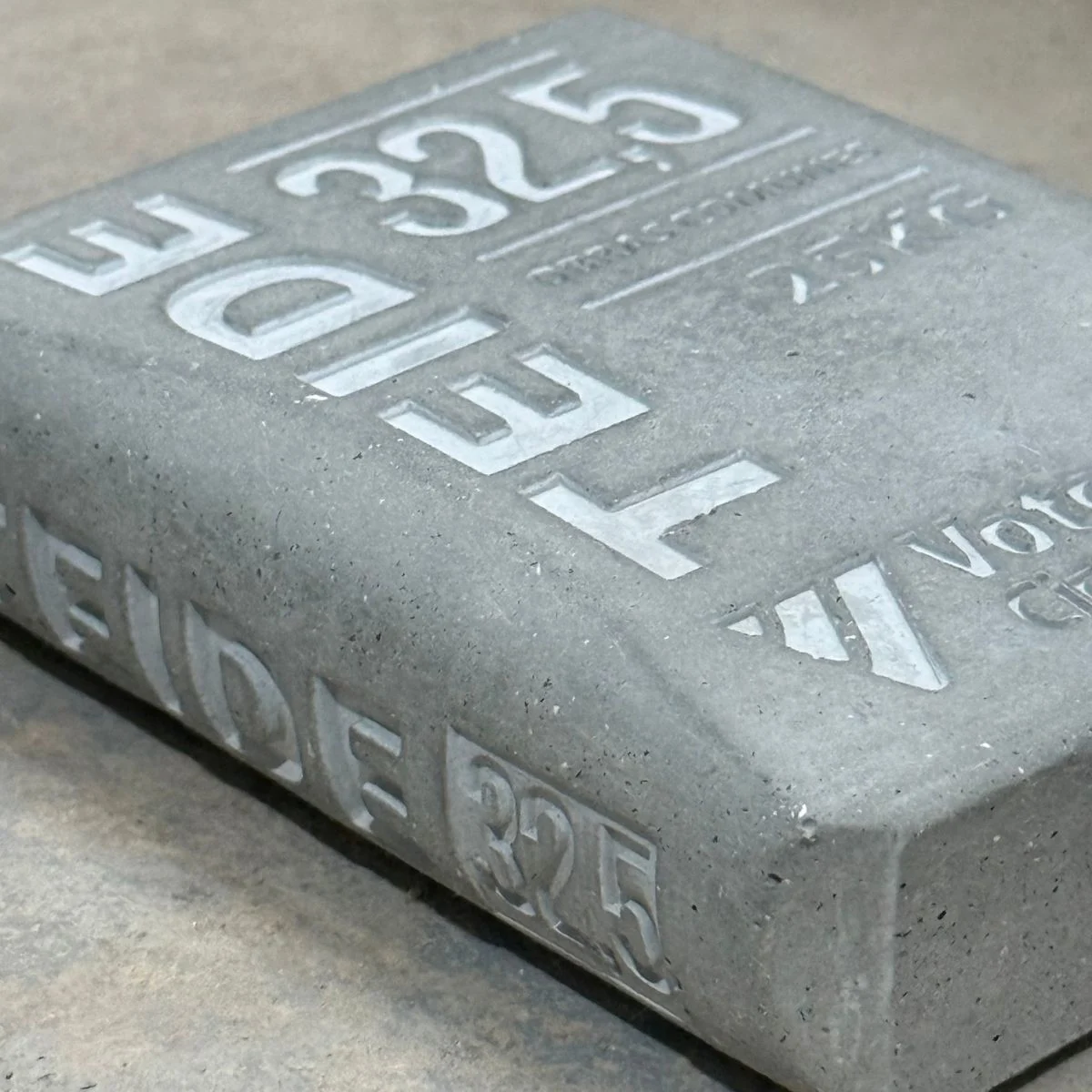 Textura y letras en relieve sobre cemento Detalle de una pieza de cemento gris con letras y números en relieve y pequeños poros en la superficie.