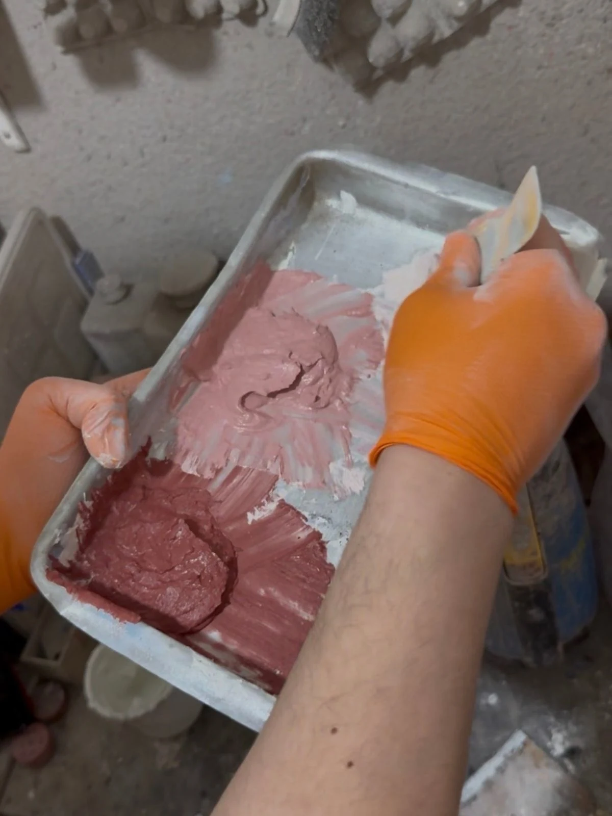 Del diseño al molde: el proceso artesanal de En Concreto Manos con guantes trabajando una mezcla rojiza en un molde en el taller de En Concreto.