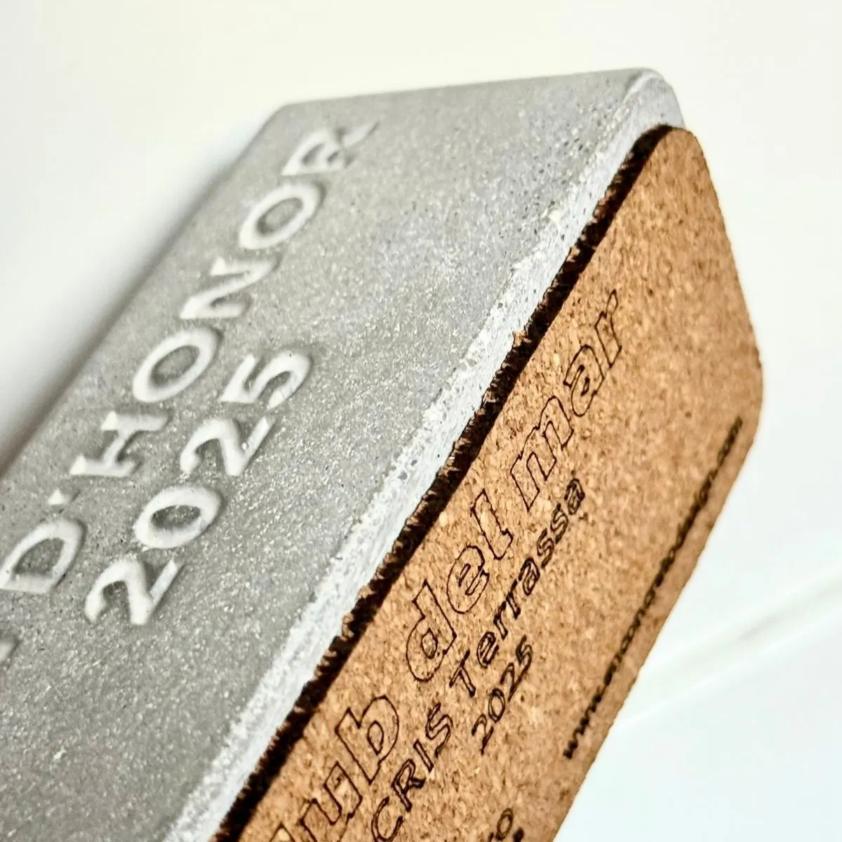 Reconocimiento personalizado de cemento con base de corcho Detalle de un reconocimiento de cemento con inscripción en relieve y una base de corcho con texto impreso.