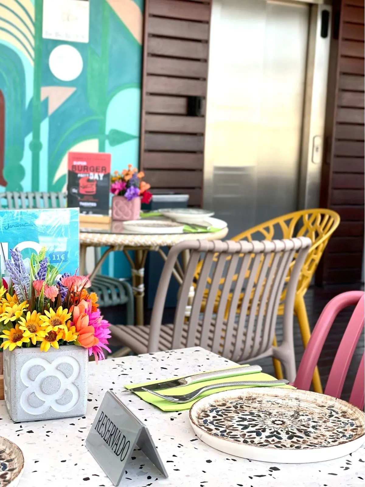 Una identidad gráfica llevada a un objeto de cemento Soporte de cemento con un símbolo gráfico sobre una mesa de terraza, junto a flores.